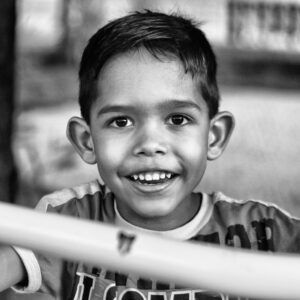 foto em preto e branco retrato em preto e branco de uma criança, cabelos lisos pretos cor da pele branca, olhos pretos e sorriso largo.